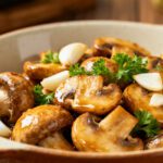 Air fryer garlic mushrooms roasted until golden brown and tender, tossed with garlic cloves, fresh parsley, and a savory buttery glaze in a serving bowl.