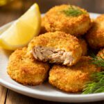 Air fryer tuna nuggets with a crispy golden breadcrumb coating and tender flaky tuna center, served with lemon wedges and fresh dill on a white plate.
