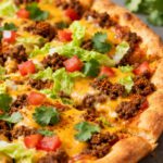 Air fryer taco pizza topped with seasoned ground beef, melted cheddar cheese, shredded lettuce, diced tomatoes, fresh cilantro, and lime wedges on a crispy pizza crust.