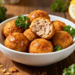 Air fryer tuna balls with a crispy golden breadcrumb coating and tender flaky tuna filling, served with lemon wedges and fresh parsley in a white bowl.