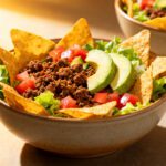 Air fryer taco salad bowls filled with seasoned ground beef, crisp lettuce, diced tomatoes, avocado slices, and tortilla chips for a fresh and flavorful meal.