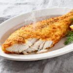 Air fryer frozen fish with a crispy golden breadcrumb coating and flaky white fish interior, served with lemon wedges and fresh dill on a white plate.