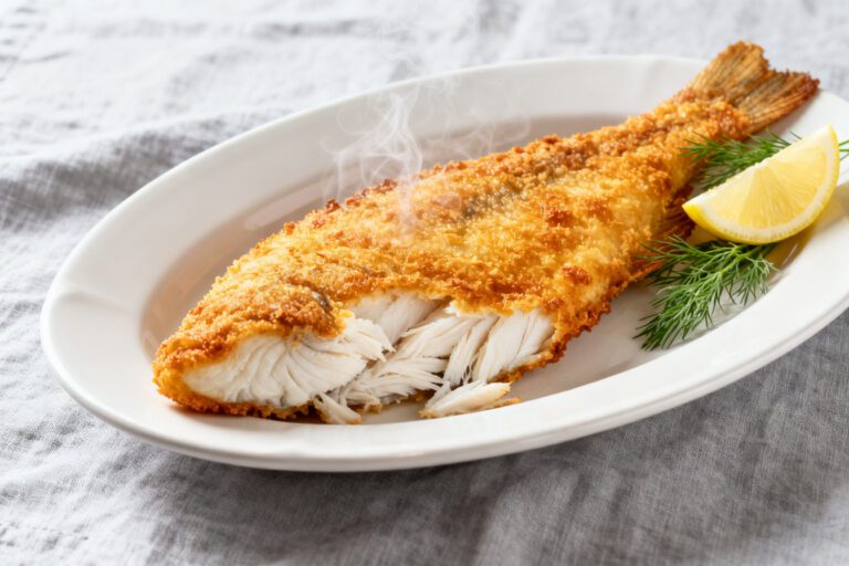 Air fryer frozen fish with a crispy golden breadcrumb coating and flaky white fish interior, served with lemon wedges and fresh dill on a white plate.