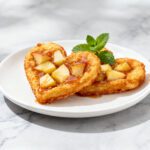 Air fryer heart shaped apple fritters with a crispy golden exterior, tender apple pieces, and a sweet glaze drizzle, served on a white plate with fresh mint.