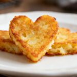 Air fryer heart shaped hash browns with a crispy golden exterior and tender potato center, served on a white plate as a cute and easy breakfast side dish.