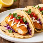 Air fryer fish tacos with crispy breaded fish, shredded purple cabbage, fresh pico de gallo, cilantro, and creamy sauce, served in warm tortillas with lime wedges.