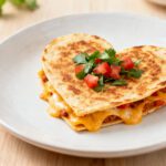 Air fryer heart shaped quesadilla with a crispy golden tortilla, melted cheese filling, and fresh diced tomatoes and cilantro on top, served as a cute and easy meal.