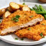 Air fryer chicken fried steak with a crispy golden breaded coating and tender steak inside, served with roasted potatoes and green beans on a dinner plate.