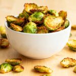 Air fryer Brussels sprout chips with crispy roasted Brussels sprout leaves and halves, lightly browned and served in a bowl as a savory and healthy snack.