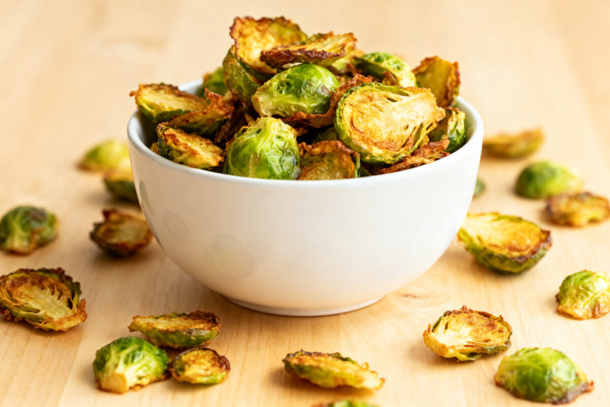 Air fryer Brussels sprout chips with crispy roasted Brussels sprout leaves and halves, lightly browned and served in a bowl as a savory and healthy snack.