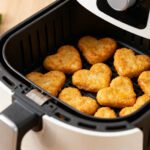 Air fryer heart shaped chicken nuggets with a crispy golden breadcrumb coating, served inside an air fryer basket with lemon wedges for a fun and kid friendly meal.