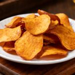 Air fryer sweet potato chips with crispy golden edges, thinly sliced sweet potatoes, and a light crunchy texture, served on a white plate as a healthy snack.