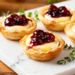 Air fryer cherry brie bites with flaky golden pastry cups filled with creamy brie cheese and topped with sweet cherry preserves, served as an elegant party appetizer.