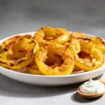 Air fryer banana pepper rings with a crispy golden coating, tangy banana peppers, and a crunchy texture, served on a plate with a creamy dipping sauce.