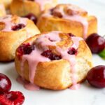Air fryer cherry breakfast rolls with soft fluffy dough, sweet cherry filling, and a pink cherry glaze, served alongside fresh cherries for a delicious breakfast treat.