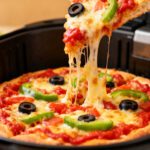 Air fryer mini frozen pizza with a crispy golden crust, melted mozzarella cheese, tomato sauce, green bell peppers, black olives, and stretchy cheese, cooking inside an air fryer basket.