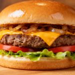 Air fryer cheeseburger with a juicy beef patty, melted cheddar cheese, caramelized onions, fresh lettuce, and tomato slices on a toasted bun.