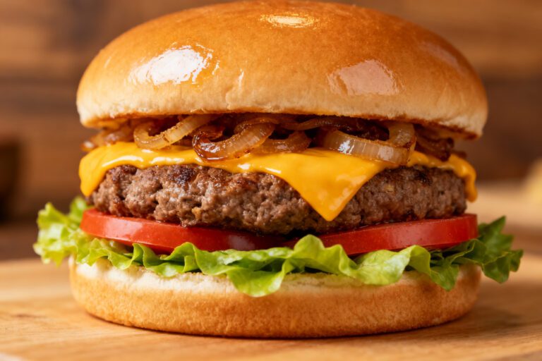 Air fryer cheeseburger with a juicy beef patty, melted cheddar cheese, caramelized onions, fresh lettuce, and tomato slices on a toasted bun.