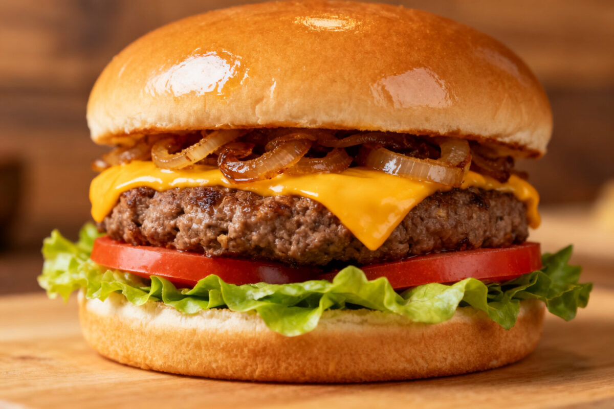 Air fryer cheeseburger with a juicy beef patty, melted cheddar cheese, caramelized onions, fresh lettuce, and tomato slices on a toasted bun.