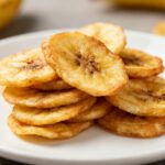 Air fryer banana chips with thinly sliced bananas cooked until crispy and lightly golden, served on a plate as a naturally sweet and healthy homemade snack.
