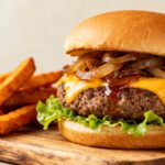 Air fryer Impossible Burger with a juicy plant based patty, melted cheddar style cheese, caramelized onions, fresh lettuce, and a toasted bun, served with crispy fries.