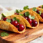 Air fryer cherry tacos with crispy golden taco shells filled with sweet cherries and fresh cilantro, served on a wooden board as a fun and creative dessert.