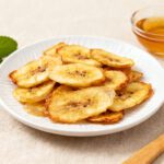 Air fryer dehydrated bananas with thin banana slices dried until lightly crisp and naturally sweet, served on a plate with honey for a simple and healthy snack.