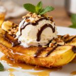 Air fryer banana split with caramelized banana halves, a scoop of vanilla ice cream, chocolate drizzle, chopped nuts, and caramel sauce, served as a warm and indulgent dessert.