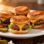 Air fryer mini burgers with juicy beef patties, melted cheddar cheese, fresh lettuce, and toasted slider buns, served on a plate as a crowd pleasing appetizer or meal.