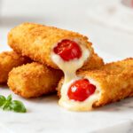Air fryer cherry mozzarella sticks with a crispy golden breadcrumb coating, gooey melted mozzarella cheese, and sweet cherry filling, served as a unique sweet and savory appetizer.