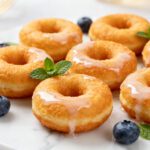 Air fryer mini donuts with a soft fluffy texture, golden exterior, sweet vanilla glaze, and fresh blueberries, served as a fun bite sized dessert or breakfast treat.