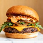 Air fryer black bean burger with a crispy black bean patty, melted cheddar cheese, caramelized onions, fresh greens, and a toasted bun, served as a hearty vegetarian meal.
