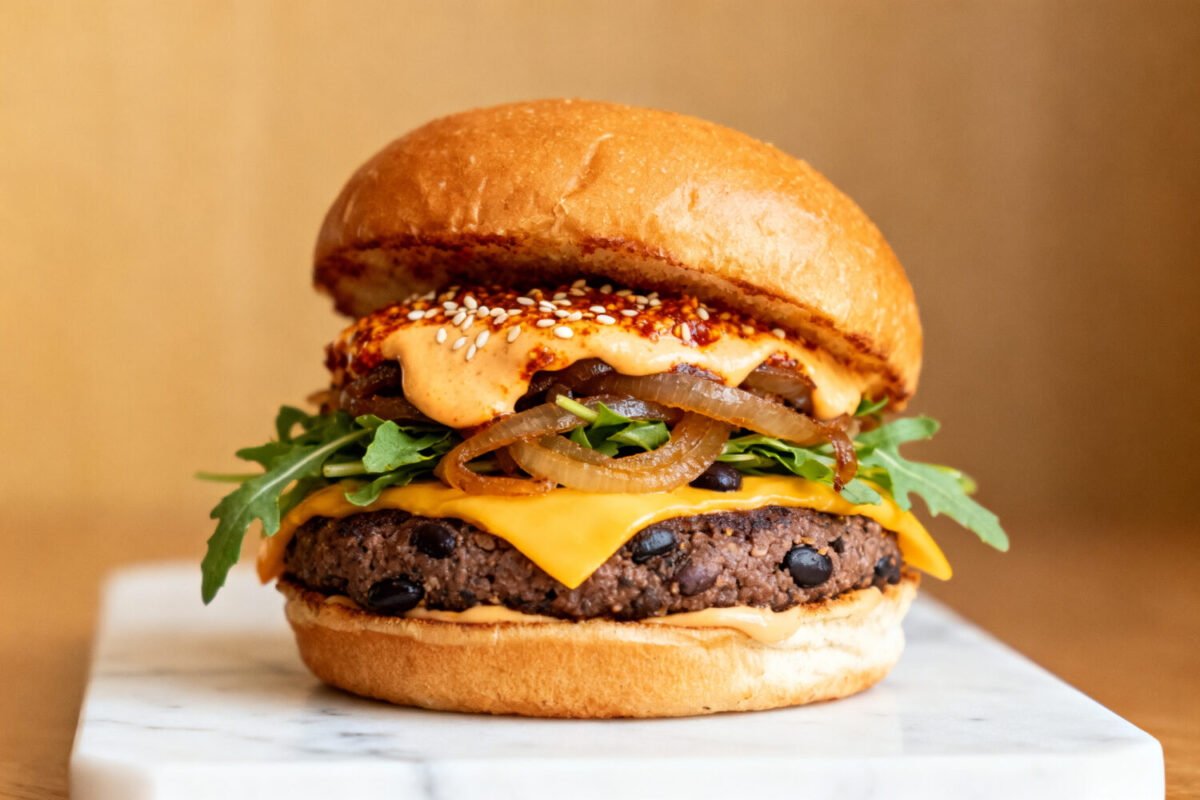 Air fryer black bean burger with a crispy black bean patty, melted cheddar cheese, caramelized onions, fresh greens, and a toasted bun, served as a hearty vegetarian meal.