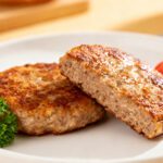 Air fryer burger patties with a juicy well seasoned beef interior, golden brown crust, and tender texture, served on a plate with fresh parsley and sliced tomato.