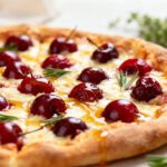 Air fryer cherry pizza with a golden crispy crust, melted cheese, sweet cherries, rosemary sprigs, and a honey drizzle, creating a unique sweet and savory twist on pizza night.