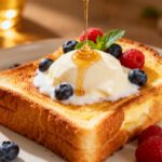 Yogurt custard toast in the air fryer with creamy baked yogurt custard, thick golden toast, fresh blueberries and raspberries, and a drizzle of honey, served as a simple sweet breakfast.