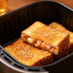 Sesame prawn toast in the air fryer with crispy golden bread coated in toasted sesame seeds and filled with savory shrimp, cooked until crunchy and golden inside an air fryer basket.