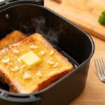 Frozen garlic toast cooked in the air fryer with a crispy golden buttery surface, toasted garlic pieces, melted butter, and steaming hot bread, served fresh from an air fryer basket.