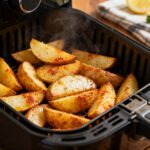 Baked potato wedges cooked in the air fryer with crispy seasoned golden edges, fluffy tender centers, and steaming hot interiors, served inside an air fryer basket as an easy side dish.