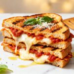 Pizza grilled cheese made in the air fryer with crispy golden toasted bread, melted mozzarella cheese, rich pizza sauce, Italian seasoning, and fresh basil, served as a cheesy comfort food sandwich.