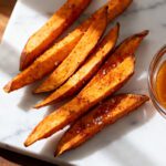 Air fryer sweet potato fries served with a creamy dipping sauce, featuring crispy roasted sweet potato wedges with caramelized edges, flaky sea salt, and a sweet and tangy glaze.