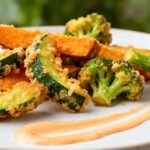 Air fryer tempura vegetables with crispy light batter, golden zucchini slices, broccoli florets, and sweet potato wedges, served with a creamy dipping sauce as a crunchy vegetable appetizer.