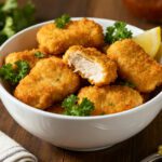 Air fryer naked chicken nuggets with a crispy golden exterior, juicy tender chicken inside, fresh parsley garnish, and lemon wedges, served as a simple high protein snack or meal.