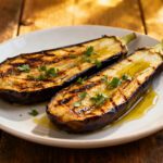 Air fryer roasted eggplant halves with tender creamy centers, lightly charred edges, olive oil, and fresh parsley garnish, served as a simple and flavorful vegetable side dish.