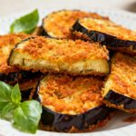 Air fryer crispy eggplant slices with a golden crunchy breadcrumb coating, tender creamy interior, fresh basil leaves, and lemon wedges, served as a light and flavorful appetizer or side dish.