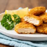 Air fryer 3 ingredient chicken nuggets with a crispy golden coating, juicy tender chicken center, fresh parsley garnish, and lemon wedges, served as a simple and family friendly meal.