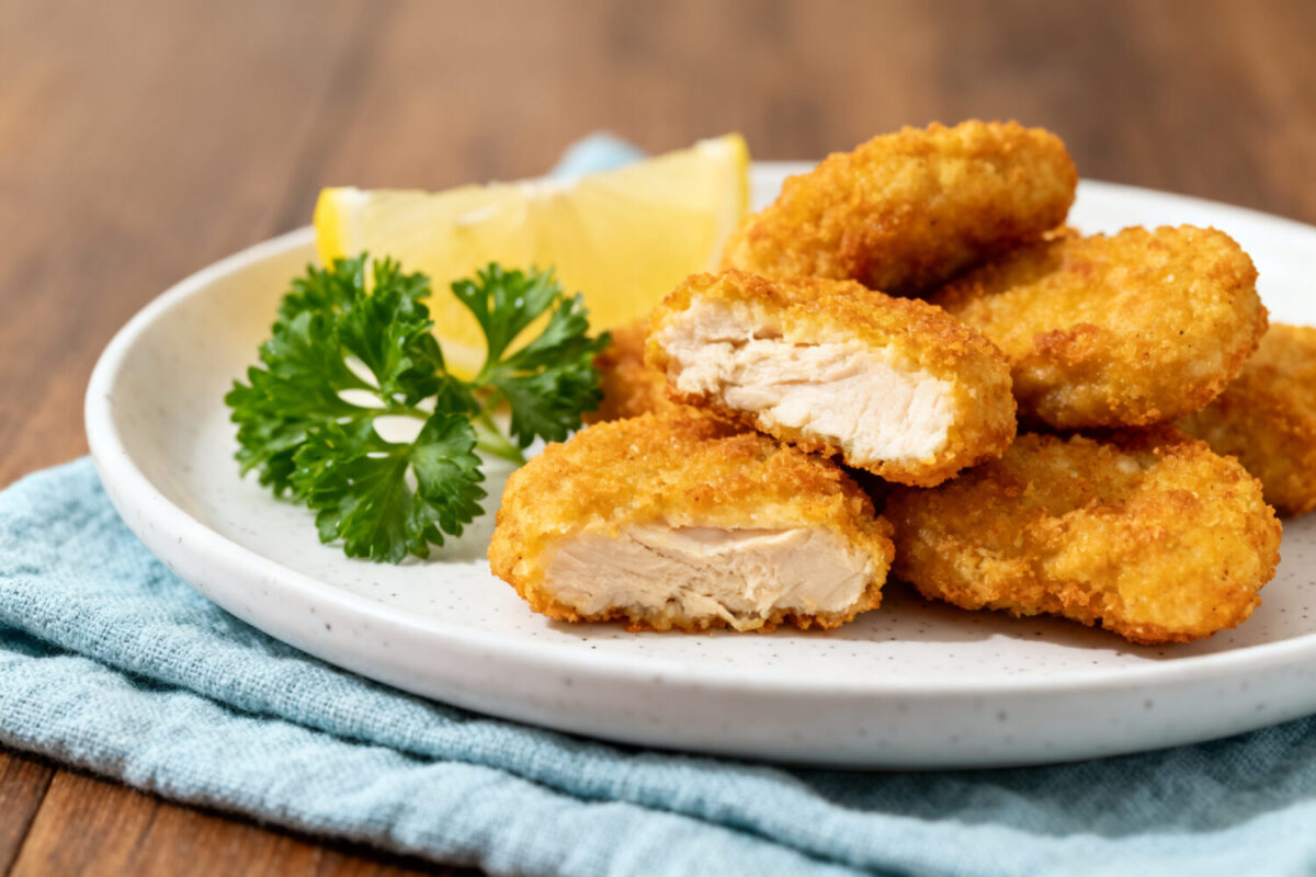Air fryer 3 ingredient chicken nuggets with a crispy golden coating, juicy tender chicken center, fresh parsley garnish, and lemon wedges, served as a simple and family friendly meal.