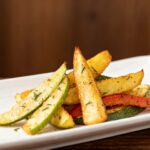Air fryer vegetables with crispy roasted zucchini, potato wedges, and bell peppers, lightly seasoned with herbs and roasted until tender crisp, served as a colorful and healthy side dish.