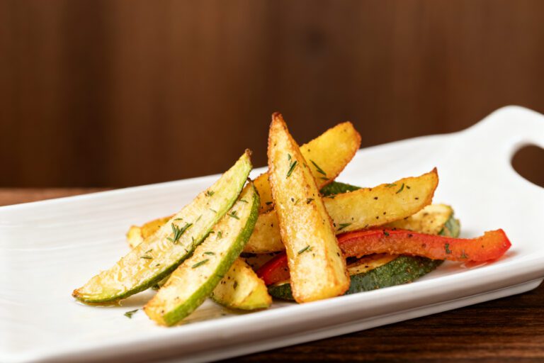Air fryer vegetables with crispy roasted zucchini, potato wedges, and bell peppers, lightly seasoned with herbs and roasted until tender crisp, served as a colorful and healthy side dish.