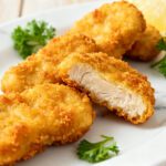 Air fryer crispy chicken nuggets with a crunchy golden breadcrumb coating, juicy tender chicken inside, fresh parsley garnish, and lemon wedges, served as an easy family friendly meal or snack.